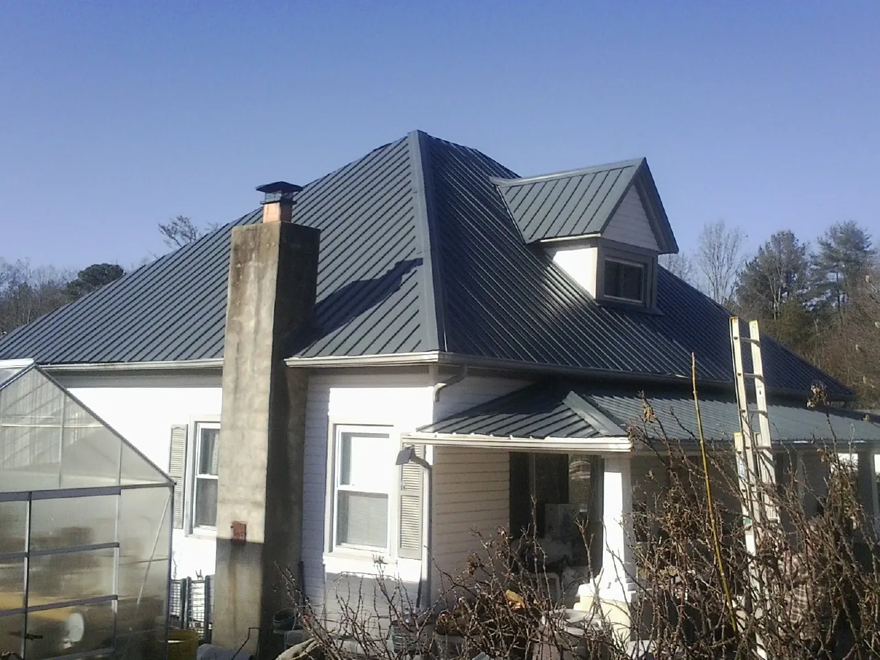 Dark blue standing seam metal roof on a white farmhouse with dormer — Slate & Tile Roof Repair by Roofing Brothers in Lehman
