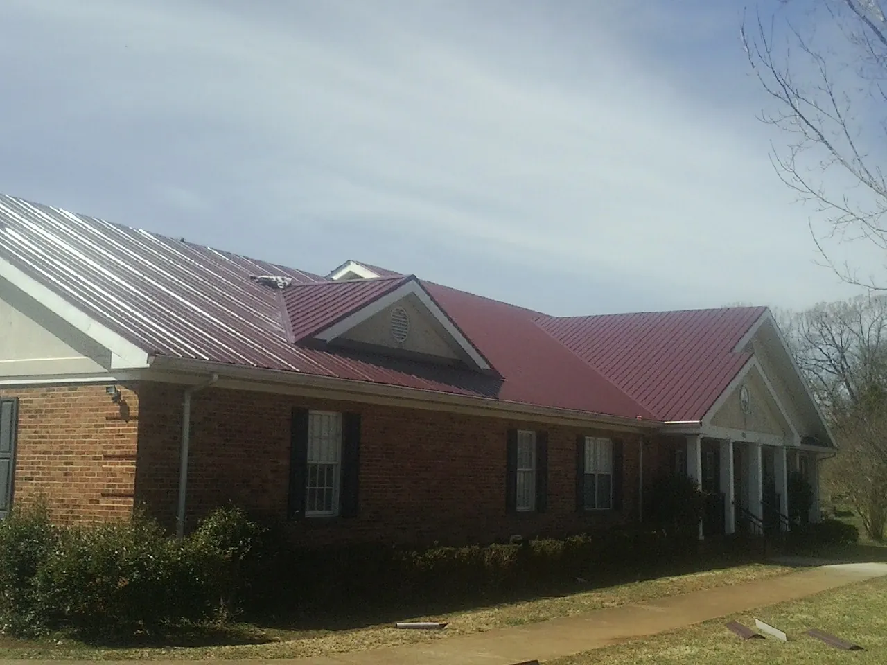 Red metal roof with gabled entries on a long brick building, from a Hail Damage Roof Repair job in Lehman
