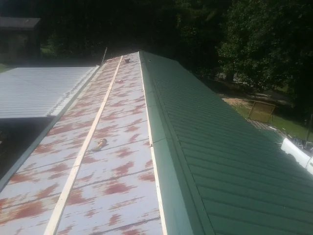 Old rusted panels beside newly installed green metal roofing — Wind Damage Roof Repair by Roofing Brothers in Lehman