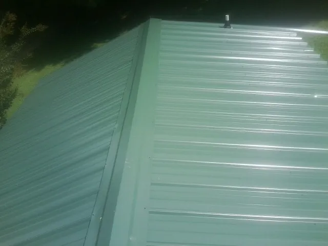 New green metal panels meeting at the ridge of a roof — Flat Roof Repair work by our crew in Lehman
