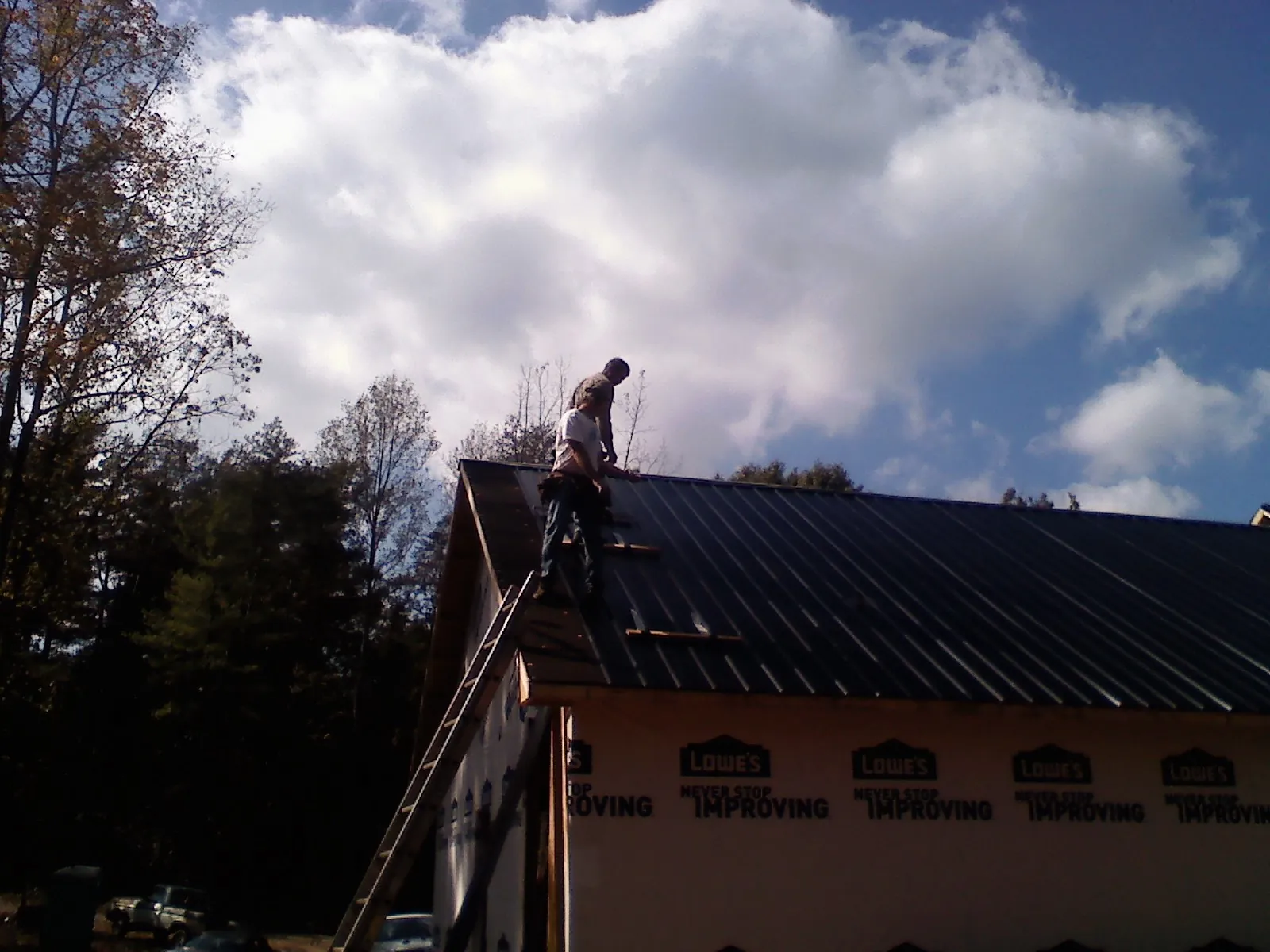 Roofer fastening dark metal panels high against a cloudy sky, from a Roof Inspection job in Lehman
