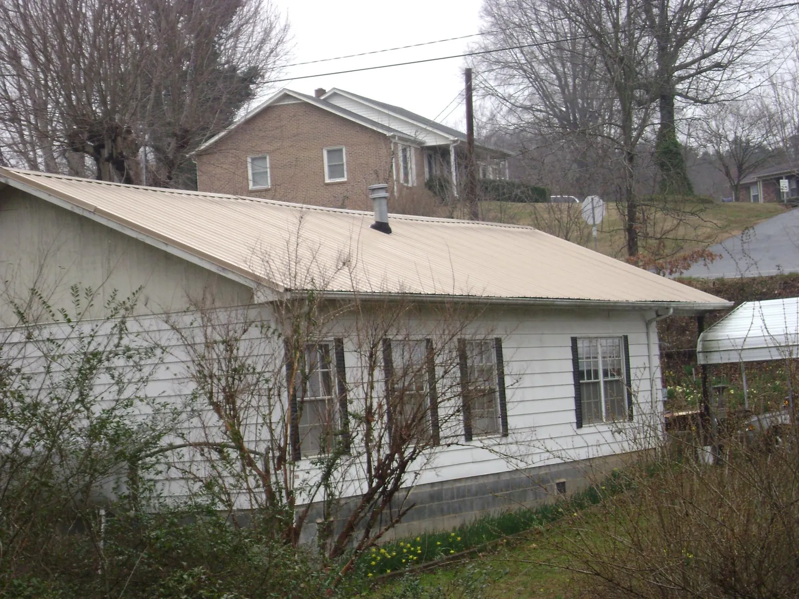 Tan metal roof on a white sided house set into a hillside — Commercial Roofing by Roofing Brothers in Lehman